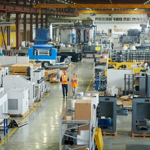 High angle full length portrait of bearded businessman wearing hardhat walking across production workshop accompanied by female factory employee, copy space