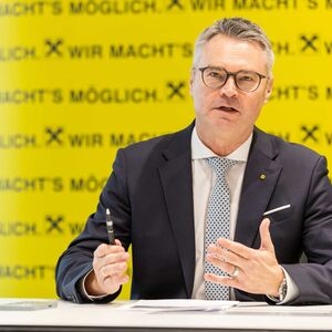 Marktvorstand Rainer Stelzer der Raiffeisen Steiermark spricht bei einer Pressekonferenz an einem Tisch sitzend,  im Hintergrund das Bankenlogo.