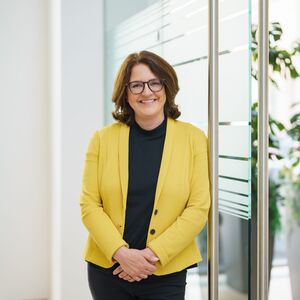 Gudrun Meierschitz, Vorständin von Acredia, lehnt gegen eine Glastür und lächelt.