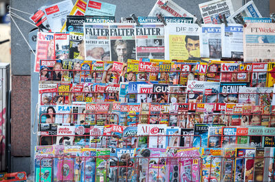 Picture of a press kiosk in the center of Vienna, Austria, filled with newspapers aligned in a magazine rack, all in German language.