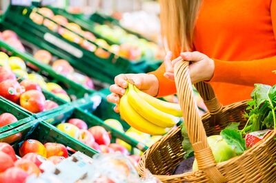 Detailansicht auf Hände einer Frau, die im Supermarkt Obst und Gemüse in einen Korb legt.