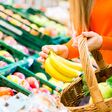 Detailansicht auf Hände einer Frau, die im Supermarkt Obst und Gemüse in einen Korb legt.
