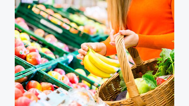 Detailansicht auf Hände einer Frau, die im Supermarkt Obst und Gemüse in einen Korb legt.