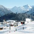 Panoramablick auf verschneiten Skihang im Skigebiet Warth am Arlberg in Österreich mit vereinzelten Skifahrern auf Piste und Sessellift