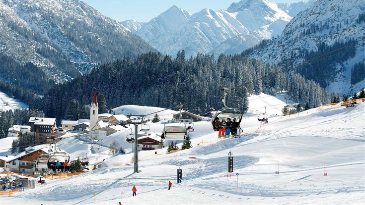 Panoramablick auf verschneiten Skihang im Skigebiet Warth am Arlberg in Österreich mit vereinzelten Skifahrern auf Piste und Sessellift
