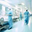 Langzeitbelichtung mit Bewegungsunschärfe von Ärztinnen, Ärzten und Pflegepersonal auf einer Krankenhausstation, die blaue Kittel tragen und durch einen Flur gehen