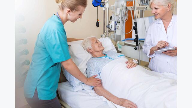 Eine alte Patientin wird im Spitalsbett von einer Krankenpflegerin und einer Ärztin betreut.