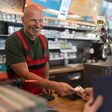 Ein älterer Mann bezahlt an der Kasse in einer Tankstelle mit Bargeld.