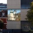 Der Uhrturm am Schlossberg spiegelt sich im Fenster eines Bürogebäudes in Graz, Steiermark.