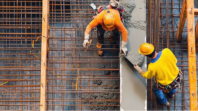 Zwei Bauarbeiter gießen Beton auf einer Baustelle.