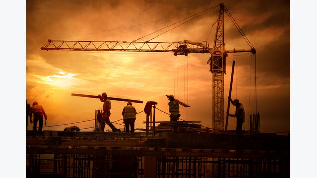 Mehrere Bauarbeiter arbeiten auf einer Baustelle mit Kran in der Abendröte.