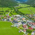 Vogelperspektive auf die Gemeinde Steeg im Naturpark Tiroler Lechtal, in Österreich: Häuser umgeben von grünen Wiesen und beginnenden Alpen.