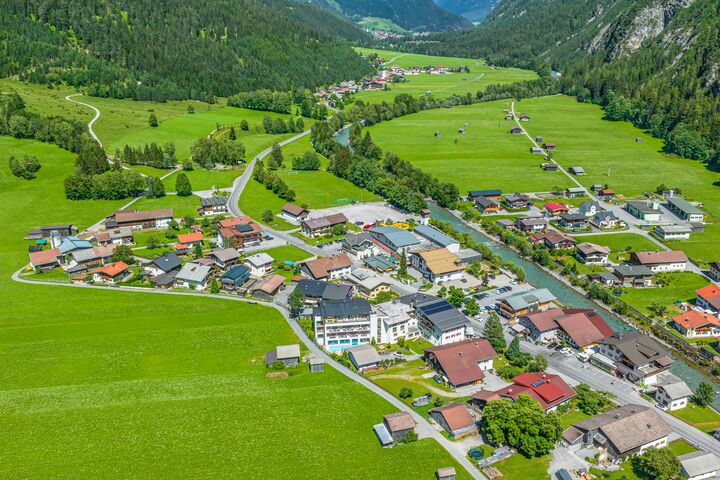 Vogelperspektive auf die Gemeinde Steeg im Naturpark Tiroler Lechtal, in Österreich: Häuser umgeben von grünen Wiesen und beginnenden Alpen.