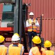 Eine Gruppe Industriearbeiter in Warnwesten und Schutzhelmen bei einer kleinen Versammlung.