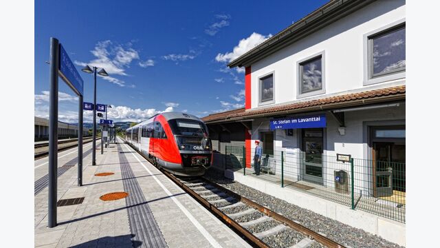 Ein roter ÖBB-Zug hält bei schönem Wetter in der Station St. Stefan im Lavanttal, die Bahnsteige sind leer.