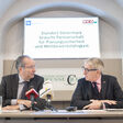 Kurt Maier, Präsident IV-Steiermark, und Josef Herk, Präsident der WK-Steiermark, sitzen bei einer Pressekonferenz gemeinsam an einem Tisch und sehen sich an.