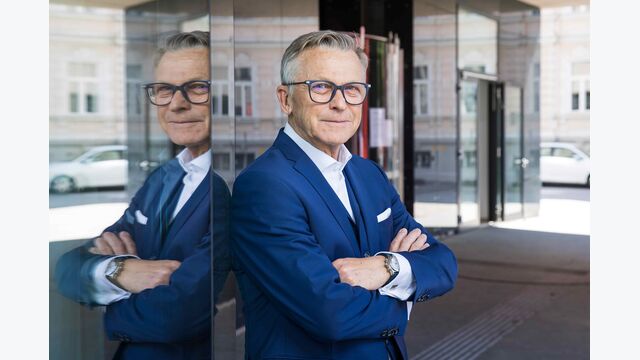 Präsident der Salzburger Wirtschaftskammer und Wirtschaftsbund-Chef Peter Buchmüller im Portrait, gegen eine spiegelnde Wand lehnend.