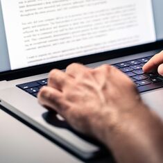 Hände schreiben an einem Textdokument an einem Laptop.