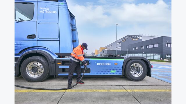Ein blauer E-Truck von Amazon wird von einem Mitarbeiter aufgeladen.