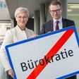 Doris Hummer, Präsidentin der WKO Oberösterreich, und Rechtsanwalt Mathis Fister, Professor an der JKU Linz, halten ein Schild, auf dem BÜROKRATIE steht, das Wort durchgestrichen.