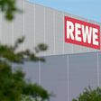 neues Zentrallager des deutschen Lebensmitteleinzelhändlers Rewe im Industriegebiet Rothensee in Magdeburg, großer roter Firmenname, das graue Gebäude hinter grünen Zweigen nur teilweise sichtbar