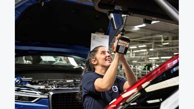 Eine lachende junge Frau arbeitet bei Volvo an einem Auto.