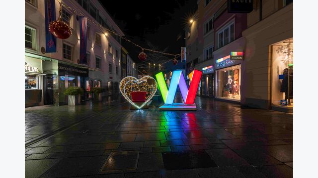 Einkaufsstraße mit Geschäftsauslagen in der Welser Innenstadt bei Nacht, im Fokus ein großes Deko-Herz und ein illuminiertes großes "W"