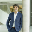 Porträt von Dr. Martin Pfeffer, Partner der Management Factory, der von der Dachorganisation Österreichisches Interim Management (DÖIM) als "Interim Manager des Jahres 2025" ausgezeichnet wurde. Auf dem Bild trägt Pfeffer einen Anzug und lehnt lächelnd gegen eine Säule in einer Eingangshalle.