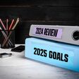 zwei dicke ordner auf einem schreibtisch, auf einem steht "2024 review", auf dem anderen "2025 goals"