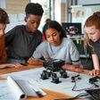 In einem Klassenzimmer arbeiten Jugendliche gemeinsam an einem Robotik-Projekt, nutzen Baupläne und Komponenten, um ihre MINT-Fähigkeiten zu verbessern.