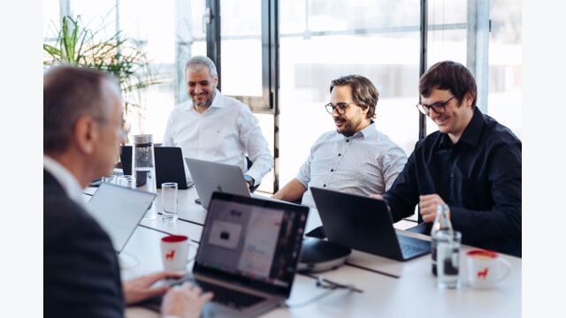 Arbeiten im Antiloop Office: Vier Männer sitzen an einem Besprechungstisch mit Laptops.