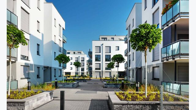 Moderne weiße Appartementgebäude mit einigen jungen Bäumen unter blauem Himmel im Sommer, menschen- und autoleere Straße.