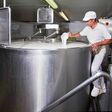 Ein Käser gießt Lab in einen großen Stahltank voller Milch.