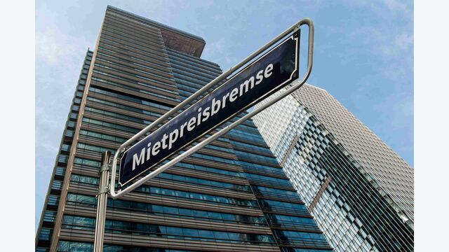 Ein Straßenschild vor einem Miethochhaus mit der Aufschrift "Mietpreisbremse".