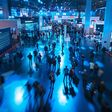Luftansicht auf herumgehende Menschenmengen in großer Messehalle in blauem Licht.