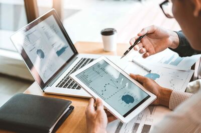 © Adobe Stock/joyfotoliakid Meeting zwischen zwei Personen an einem Schreibtisch mit Geschäftsberichten und Statistiken auf Laptop und Tablet