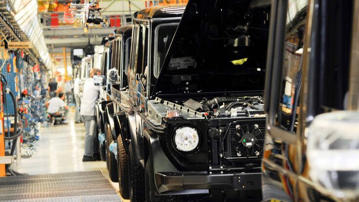 © elmar gubisch Eine Reihe schwarzer Mercedes G-Klasse in der Produktion, im Hintergrund verschwommen Techniker.
