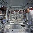 Arbeiter werken an einem chromfarbenen Rohbau eines Autos in Industrieumgebung.