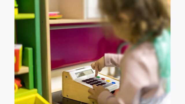Ein verschwommen sichtbares Kind spielt mit einer Spielzeugkasse.