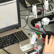 Kinderhand auf einer Computermaus neben Laptop, auf dem Mindstorm zu sehen ist.