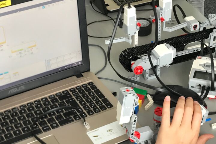 Kinderhand auf einer Computermaus neben Laptop, auf dem Mindstorm zu sehen ist.