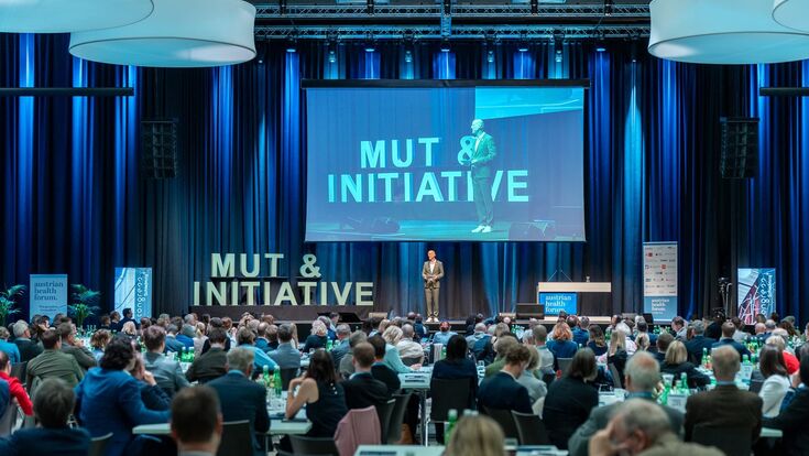 © AHF Austrian Health Forum 2025 in Schladming, mit versammelten Publikum vor Bühne mit großer Leinwand.