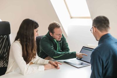© Senseven GmbH Zwei Männer und eine Frau sitzen gemeinsam an einem Tisch und blicken auf einen Laptop