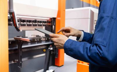 © Adobe Stock/ scharfsinn86 Eine Person steuert Maschinen in einer smarte Fabrik mithilfe eines digitalen Tablets.