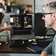 Ein junger und ein etwas älterer Mann bei der Programmierarbeit am Computer im Büro: Der jüngere erklärt dem älteren etwas und deutet auf ein laufendes Programm am Laptop
