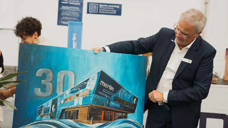 Merlin Technology-Gründer Johann Reisinger betrachtet gemaltes Bild seines Firmgebäudes
