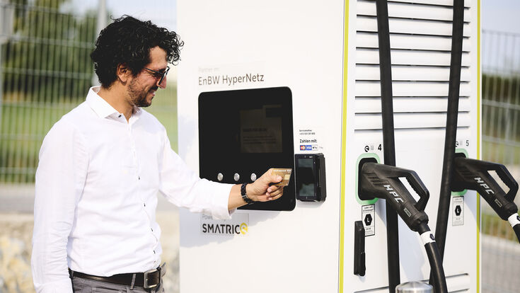 Mann zahlt bei E-Auto-Ladesäule mit Kreditkarte