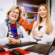 Zwei Frauen an einem Infostand mit offenem Laptop bewerben  „Digital Überall“-Workshops im Digital-Angebot der Stadt Leoben.