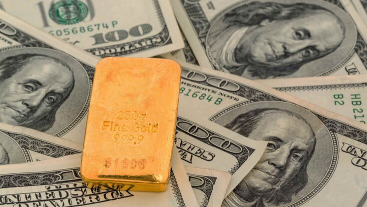 Eine Goldbarren liegt auf einem Haufen Dollarscheine.