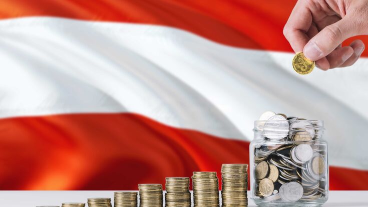 höher wachsende Türme aus Münzen, am Ende der Reihe ein Glas voll Münzen, das von einer Hand gefüllt wird; im Hintergrund die Österreich-Flagge